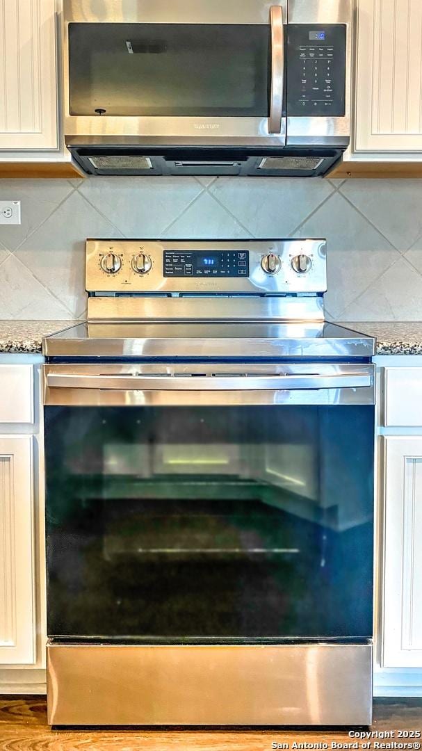 interior details with stainless steel appliances, light stone countertops, tasteful backsplash, and white cabinetry