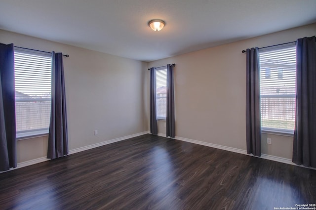 empty room with a healthy amount of sunlight, dark wood-style flooring, and baseboards