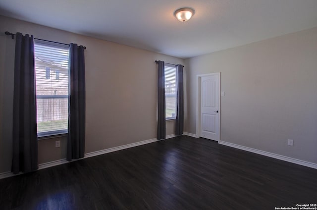 spare room with baseboards and dark wood-style flooring