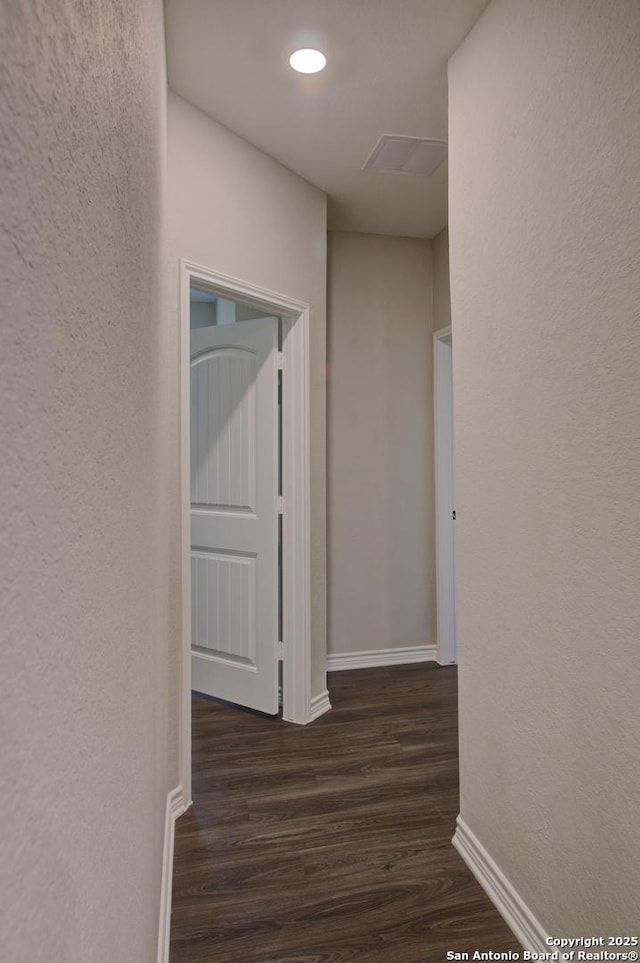 hall featuring baseboards, dark wood-type flooring, and a textured wall