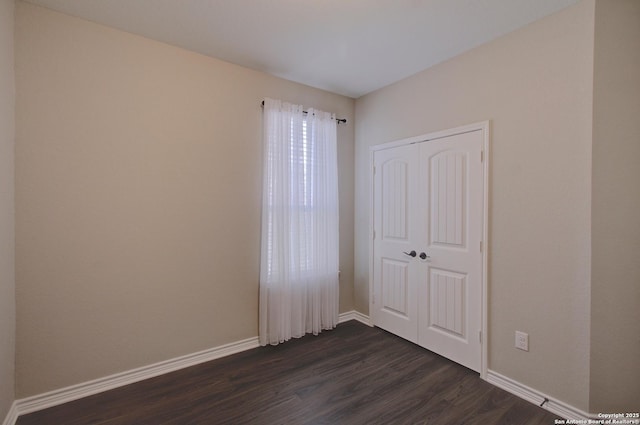 unfurnished bedroom featuring dark wood finished floors, a closet, and baseboards