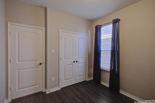 unfurnished bedroom with dark wood finished floors, baseboards, and a closet