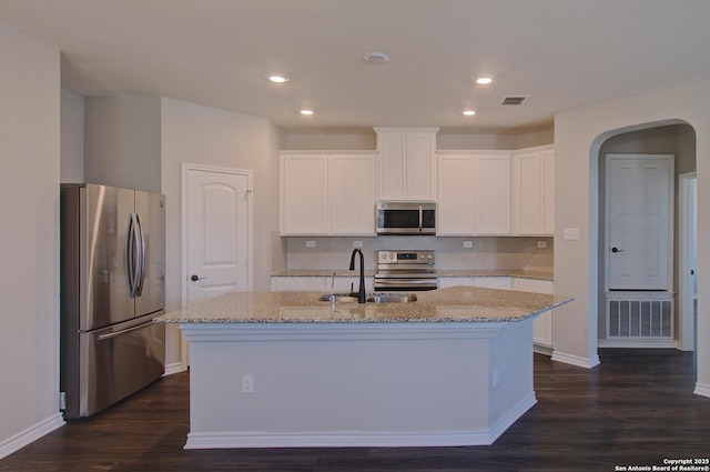 kitchen featuring light stone countertops, a kitchen island with sink, arched walkways, a sink, and appliances with stainless steel finishes