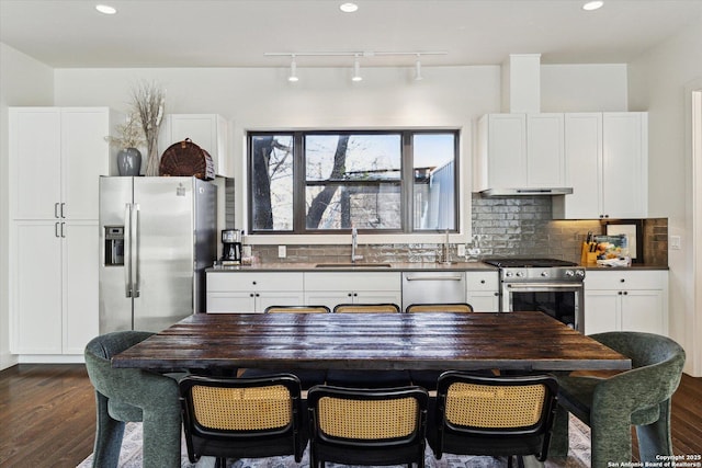 kitchen with under cabinet range hood, a sink, dark countertops, dark wood finished floors, and appliances with stainless steel finishes