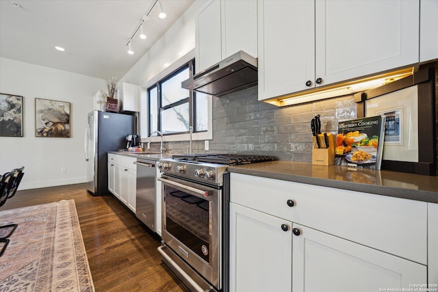 kitchen with dark wood-style floors, a sink, decorative backsplash, under cabinet range hood, and appliances with stainless steel finishes