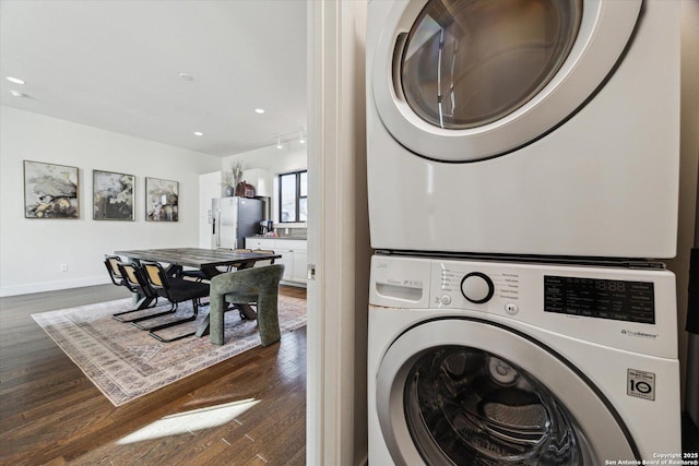 clothes washing area with laundry area, stacked washer / dryer, dark wood-style floors, and baseboards