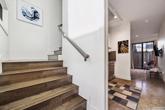 stairway featuring rail lighting, baseboards, and concrete floors