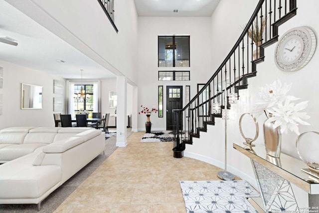 tiled entrance foyer featuring baseboards, a high ceiling, an inviting chandelier, and stairs