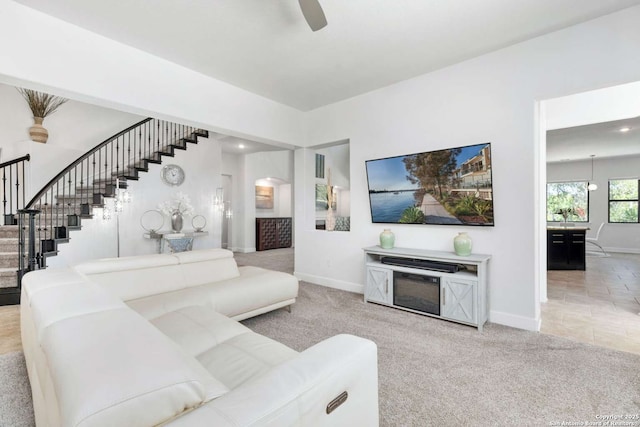 carpeted living room with baseboards, ceiling fan, and stairs