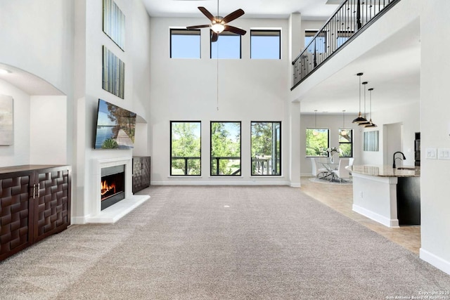 unfurnished living room featuring ceiling fan, baseboards, carpet, a lit fireplace, and a sink