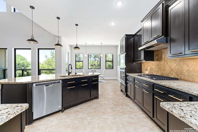 kitchen with tasteful backsplash, under cabinet range hood, pendant lighting, appliances with stainless steel finishes, and a sink