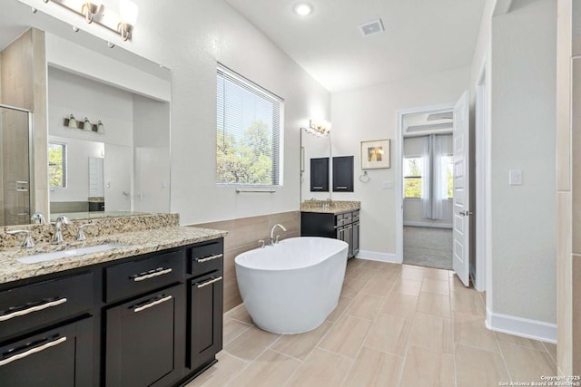 full bath with visible vents, a soaking tub, two vanities, a sink, and a shower stall