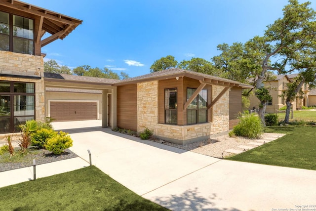 view of front of house with stone siding, a front yard, concrete driveway, and an attached garage