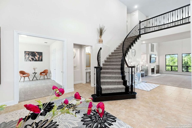 carpeted foyer entrance featuring stairway, baseboards, a fireplace with raised hearth, a towering ceiling, and tile patterned floors