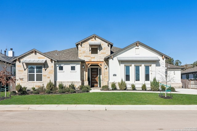 view of front facade featuring stone siding, a shingled roof, a front yard, and fence