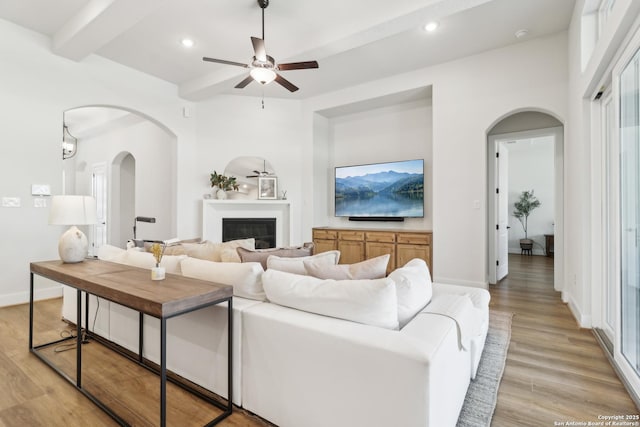 living area featuring a glass covered fireplace, beam ceiling, recessed lighting, and light wood finished floors