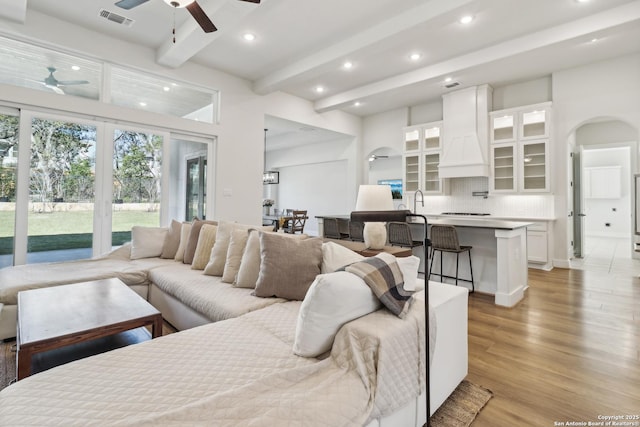 living area featuring visible vents, beam ceiling, arched walkways, ceiling fan, and light wood-type flooring