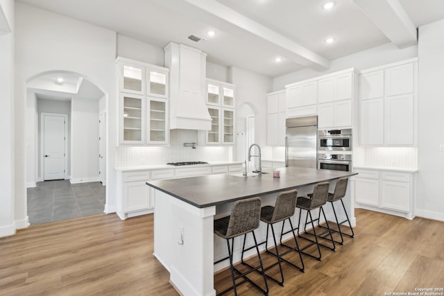 kitchen featuring arched walkways, beam ceiling, stainless steel appliances, and a sink