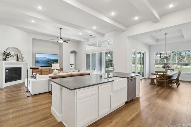 kitchen with a sink, dark countertops, a glass covered fireplace, white cabinets, and dishwasher