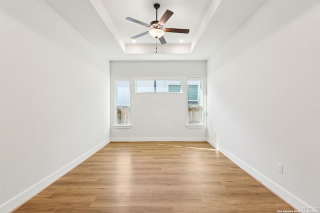 spare room with light wood-type flooring, a raised ceiling, and baseboards