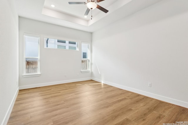 empty room featuring a raised ceiling, a ceiling fan, recessed lighting, light wood finished floors, and baseboards