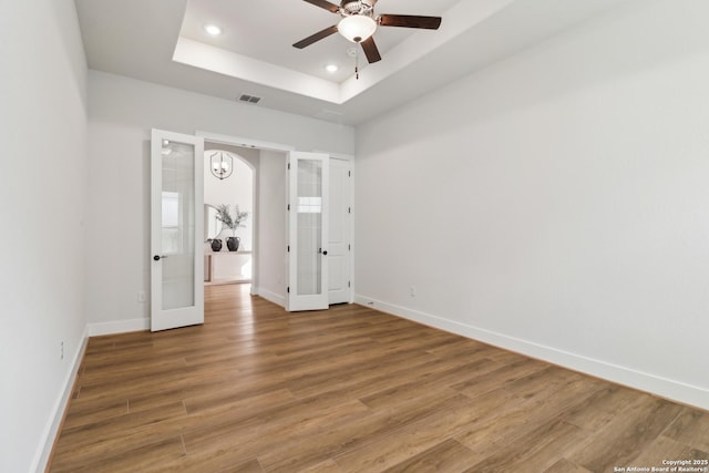 unfurnished bedroom featuring visible vents, baseboards, a tray ceiling, and wood finished floors