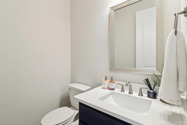 half bath with toilet, vanity, and a textured wall