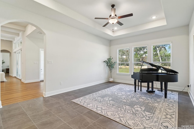 living area with a raised ceiling, recessed lighting, baseboards, and arched walkways