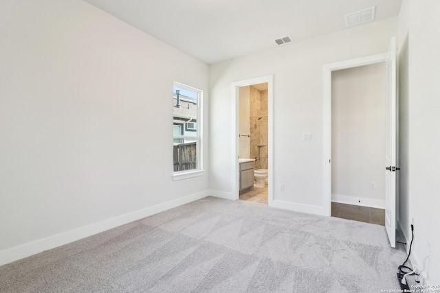 unfurnished bedroom with visible vents, baseboards, light colored carpet, and ensuite bathroom