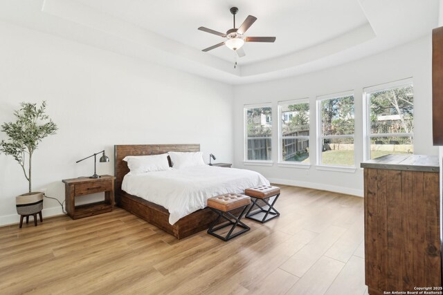 bedroom with light wood finished floors, a ceiling fan, a raised ceiling, and baseboards