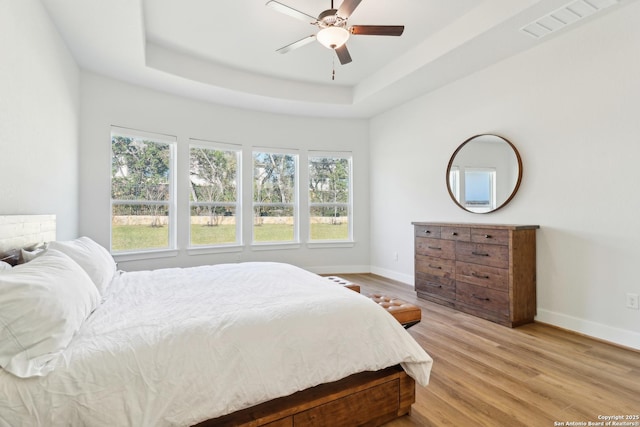 bedroom with a raised ceiling, visible vents, baseboards, and light wood finished floors