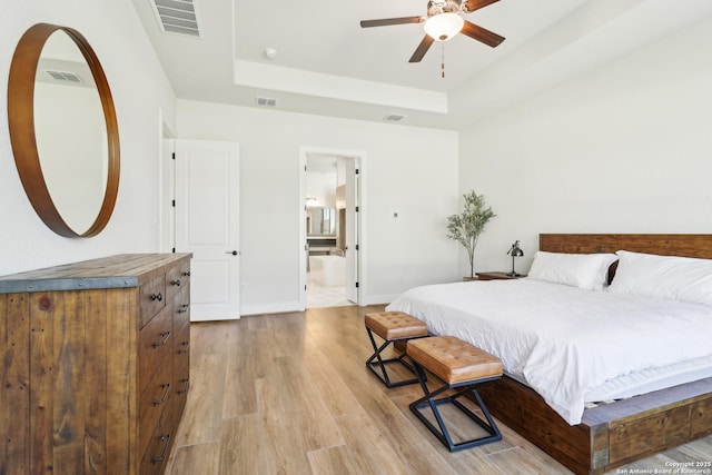 bedroom featuring a tray ceiling, light wood-style floors, and visible vents