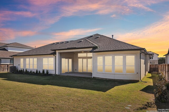 back of house at dusk featuring a patio area, a yard, a fenced backyard, and stucco siding