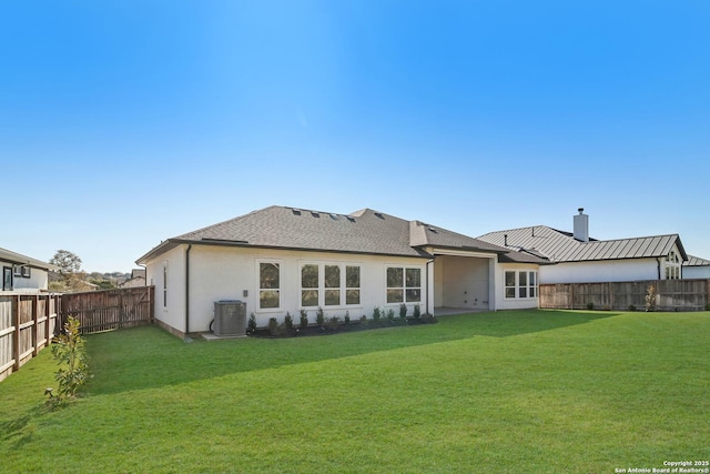 rear view of property featuring central AC unit, roof with shingles, a fenced backyard, stucco siding, and a lawn