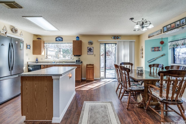 kitchen featuring visible vents, a sink, a center island, freestanding refrigerator, and dark wood-style flooring