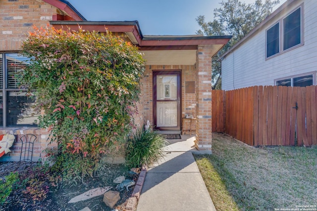 entrance to property featuring brick siding, a lawn, and fence