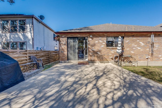 rear view of property featuring a patio, fence, brick siding, and a shingled roof