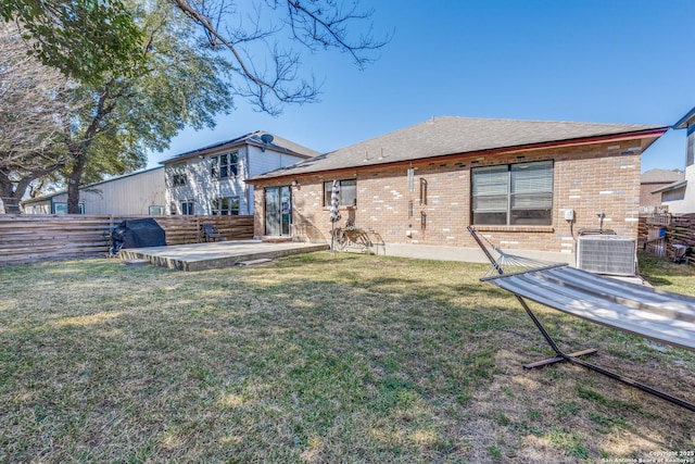 rear view of house with brick siding, a lawn, cooling unit, and fence