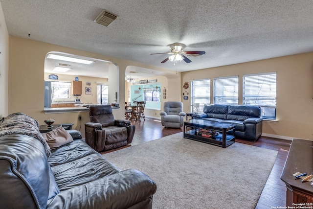 living room featuring visible vents, a textured ceiling, baseboards, and wood finished floors