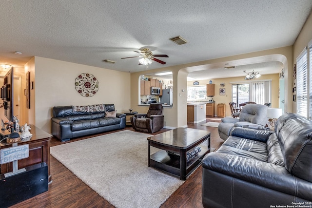 living area with visible vents, arched walkways, a textured ceiling, and dark wood-style flooring