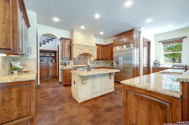 133 Fair Spgs, Boerne, TX 78006 - kitchen with stainless steel built in refrigerator, a sink, finished concrete floors, custom exhaust hood, and tasteful backsplash