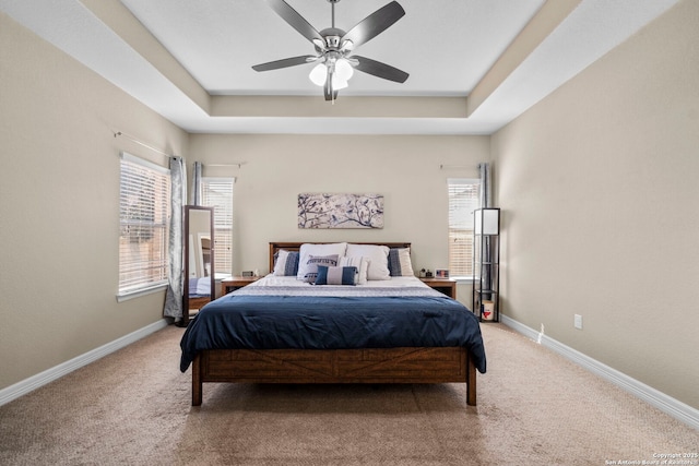 bedroom featuring baseboards, a raised ceiling, light carpet, and a ceiling fan