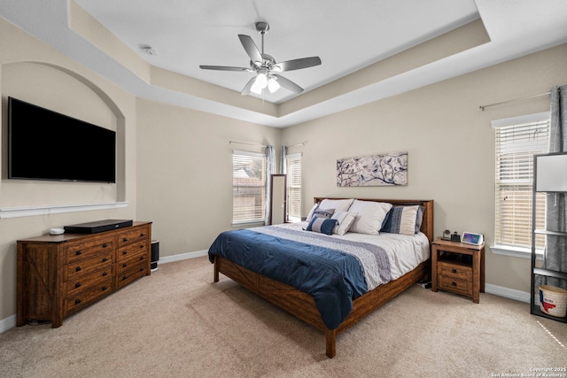 bedroom with a tray ceiling, light colored carpet, baseboards, and ceiling fan