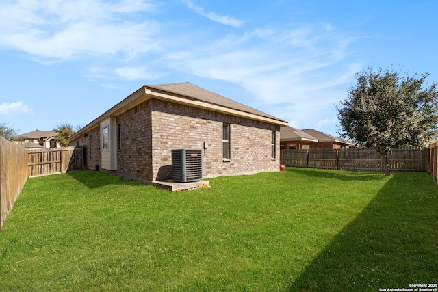 back of property with brick siding, central air condition unit, a fenced backyard, and a yard