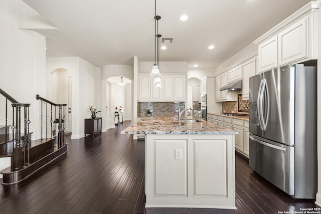 kitchen featuring dark wood finished floors, arched walkways, a sink, under cabinet range hood, and appliances with stainless steel finishes