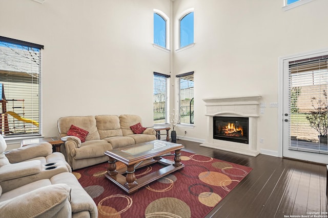 living room featuring a glass covered fireplace, a towering ceiling, baseboards, and wood-type flooring