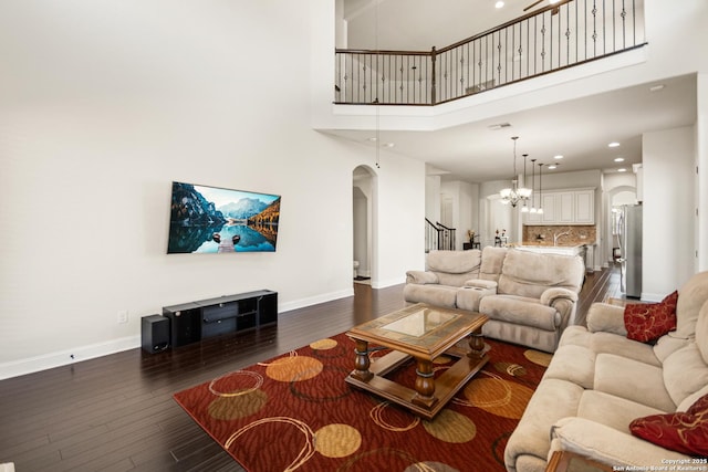 living area featuring baseboards, arched walkways, dark wood-style flooring, stairs, and a chandelier