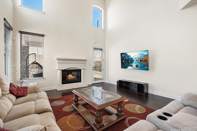 living area featuring a glass covered fireplace, dark wood-type flooring, a high ceiling, and baseboards