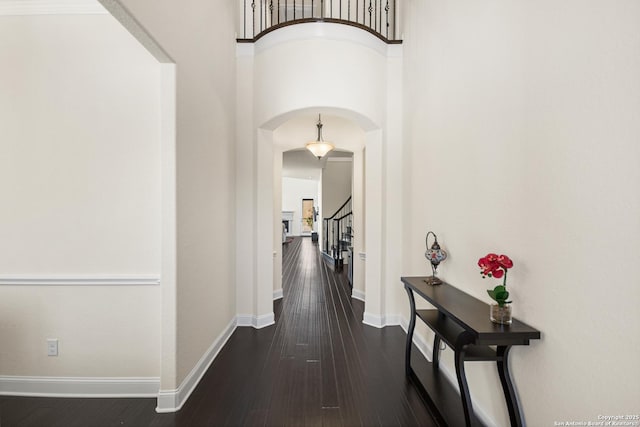 hallway featuring dark wood finished floors, arched walkways, a high ceiling, baseboards, and stairs