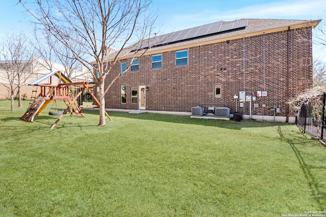 back of house featuring playground community, central AC unit, a lawn, and brick siding